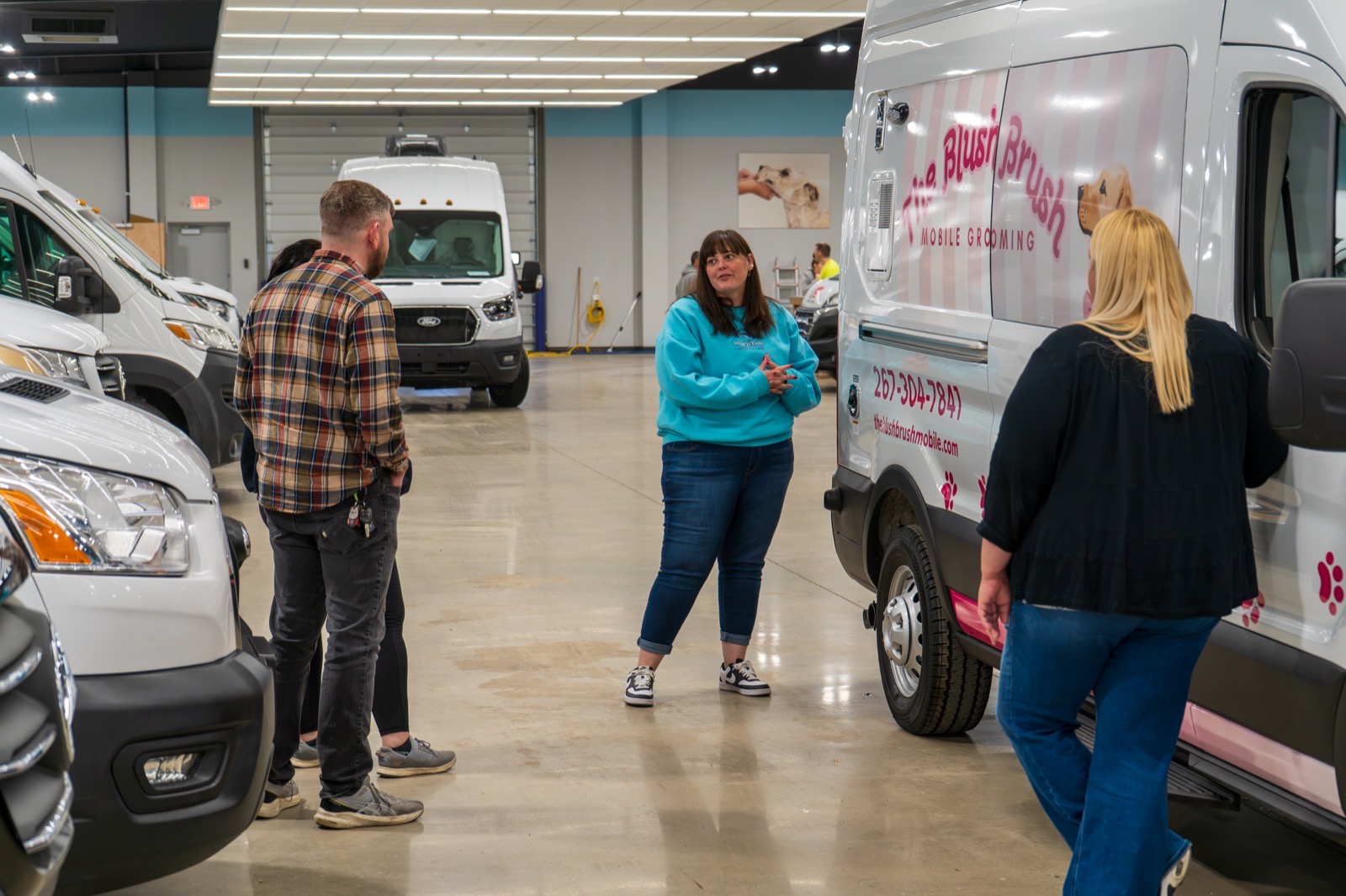 Wag'n Tails team walking a new owner through their wrapped mobile grooming van in the Granger showroom