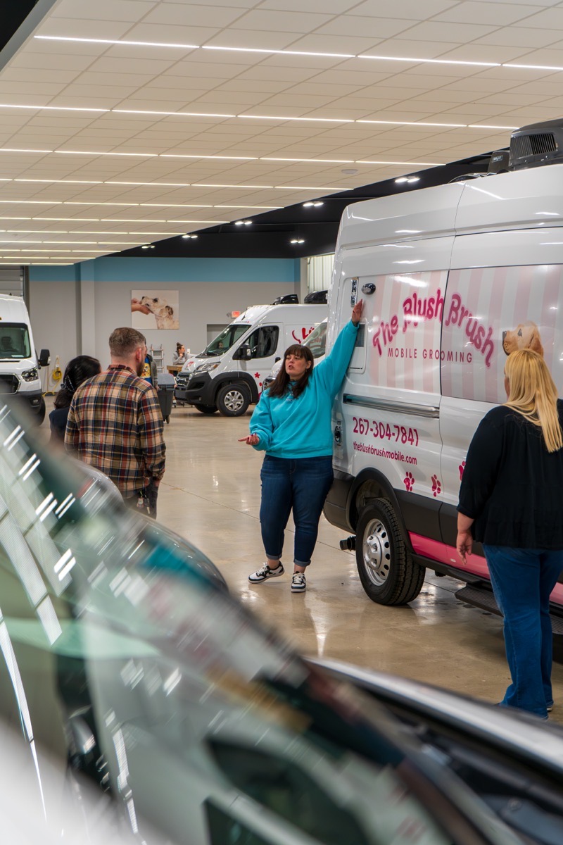 Wag'n Tails teammate presenting a newly wrapped Plush Brush grooming van in the showroom