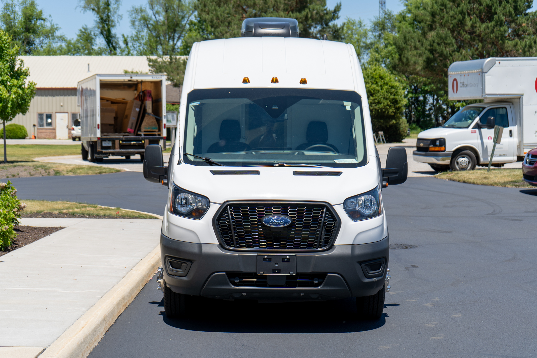 Front view of a white Ford cargo van parked in a lot, with loading trucks in the background on either side.