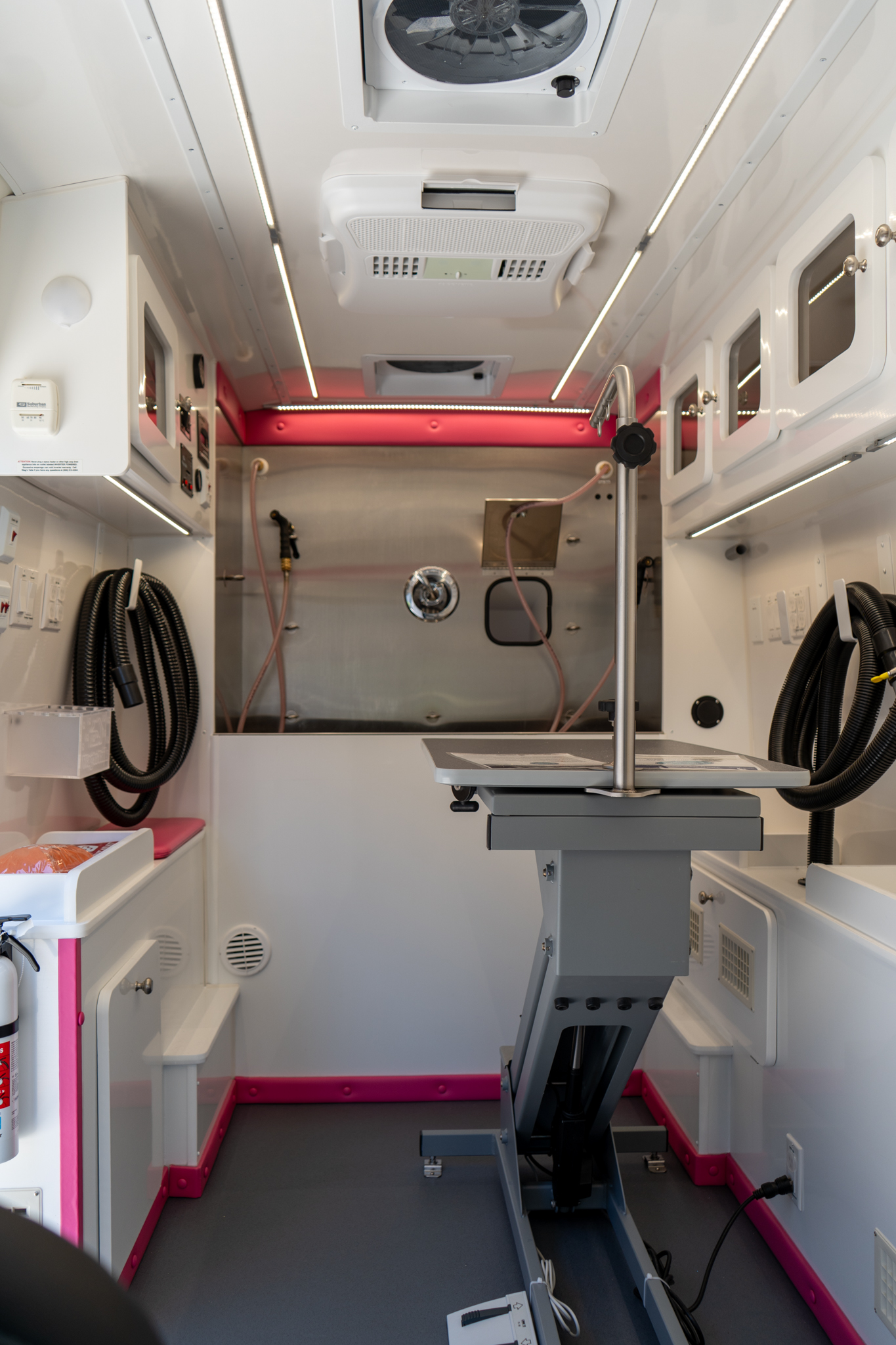 Interior of a medical ambulance with a central patient stretcher and overhead vents; white walls with pink trim along the bottom edge.