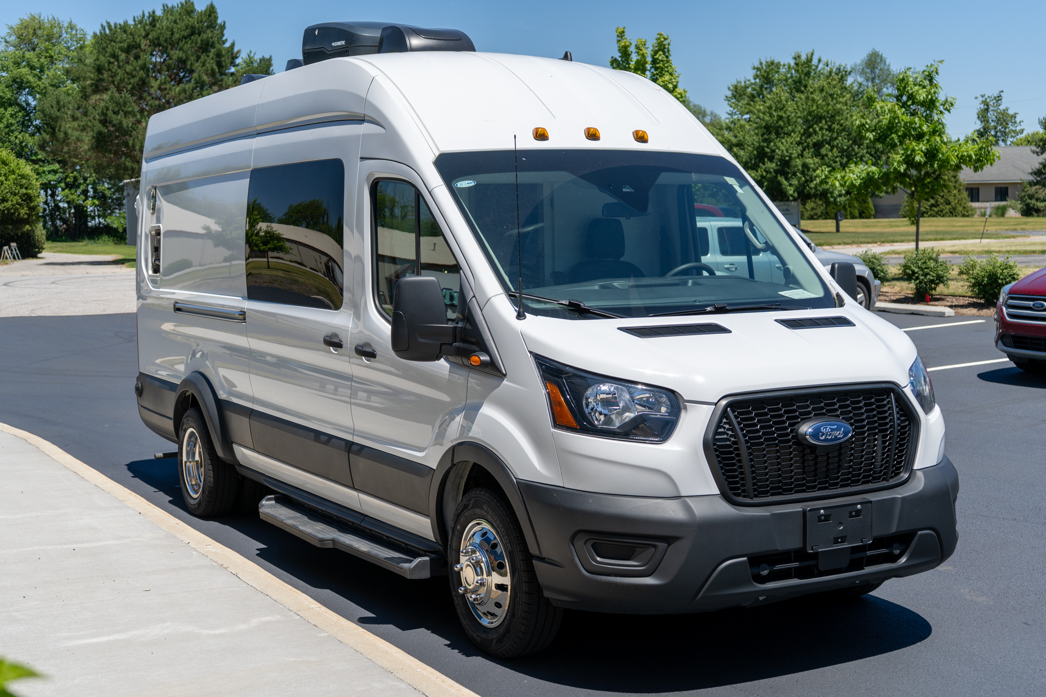 White van seen from a front-side angle parked in a sunny parking lot, with a rooftop cargo box on top.