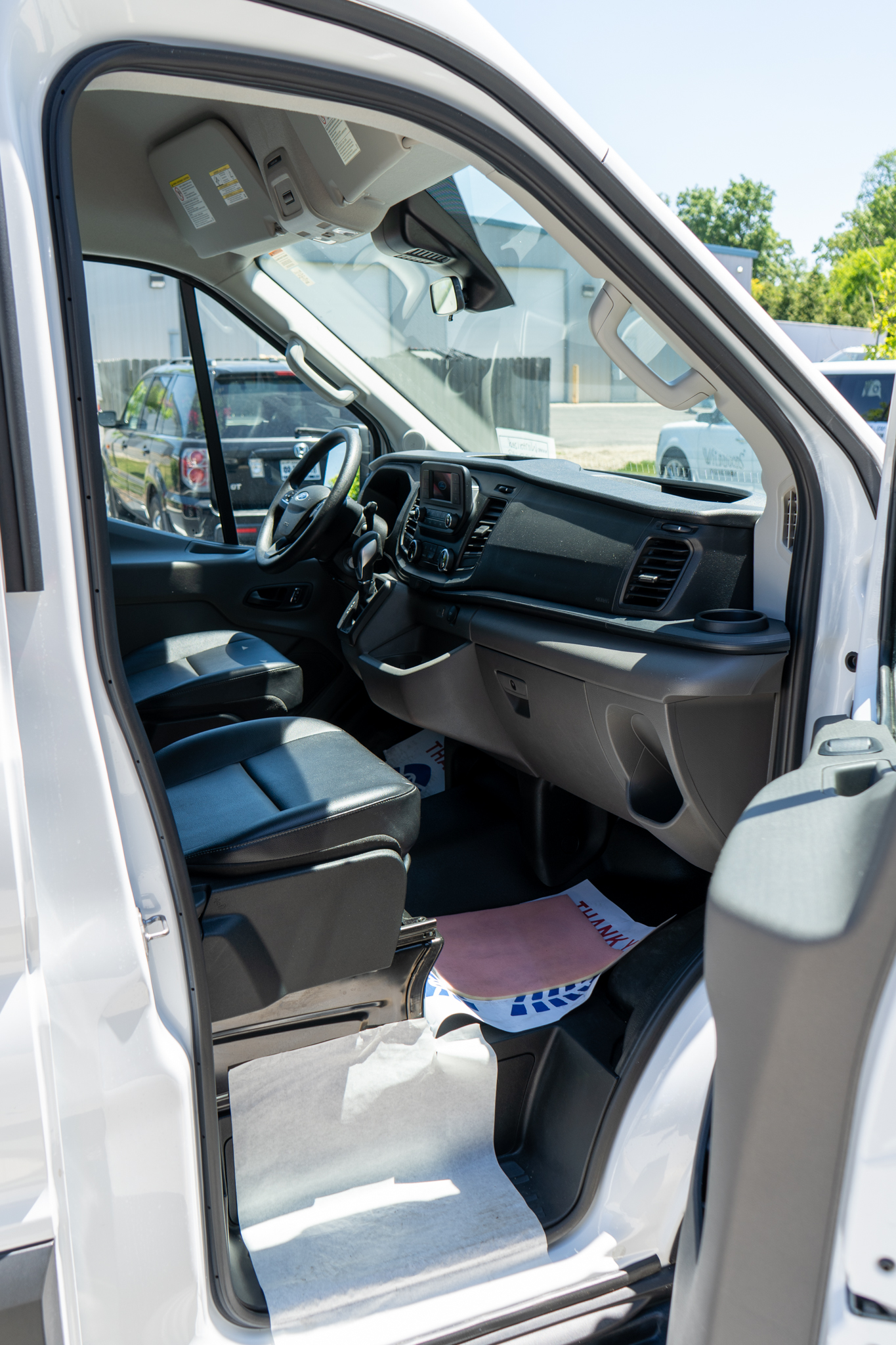 Open driver's-side door reveals the van's front cab with steering wheel, dashboard, and center console visible under bright daylight.