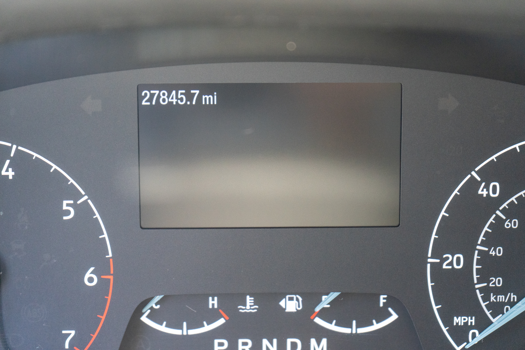 Close-up of a car dashboard showing an odometer reading 27,845.7 miles and partial speedometer and tachometer dials.