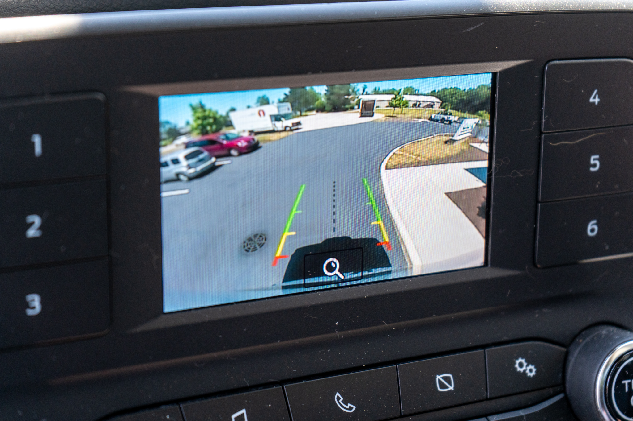 Rearview camera display showing parking lot with guide lines for reversing into a space.