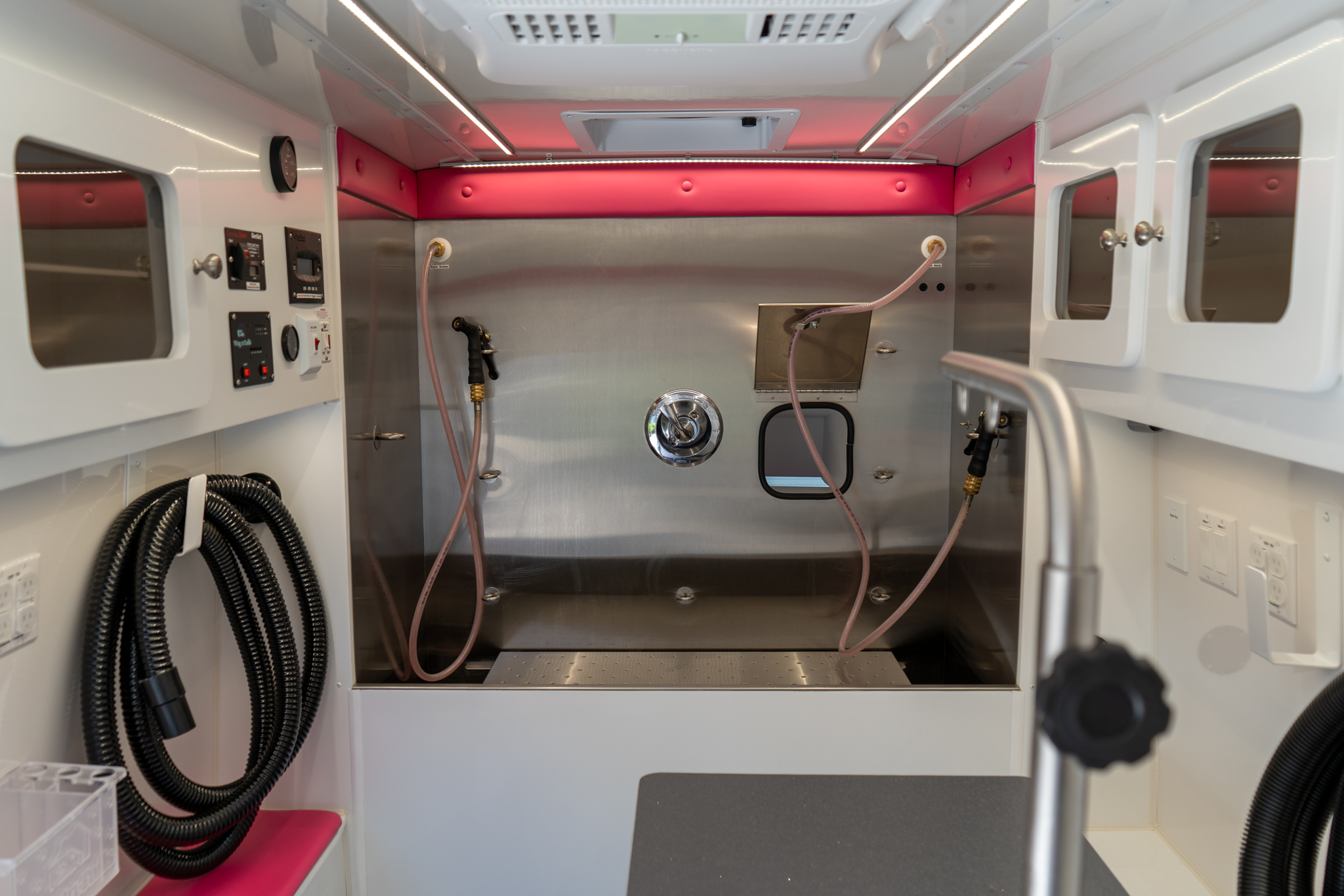 Interior of a mobile clinic room with pink cushioned wall, stainless steel panels, and hanging hoses.