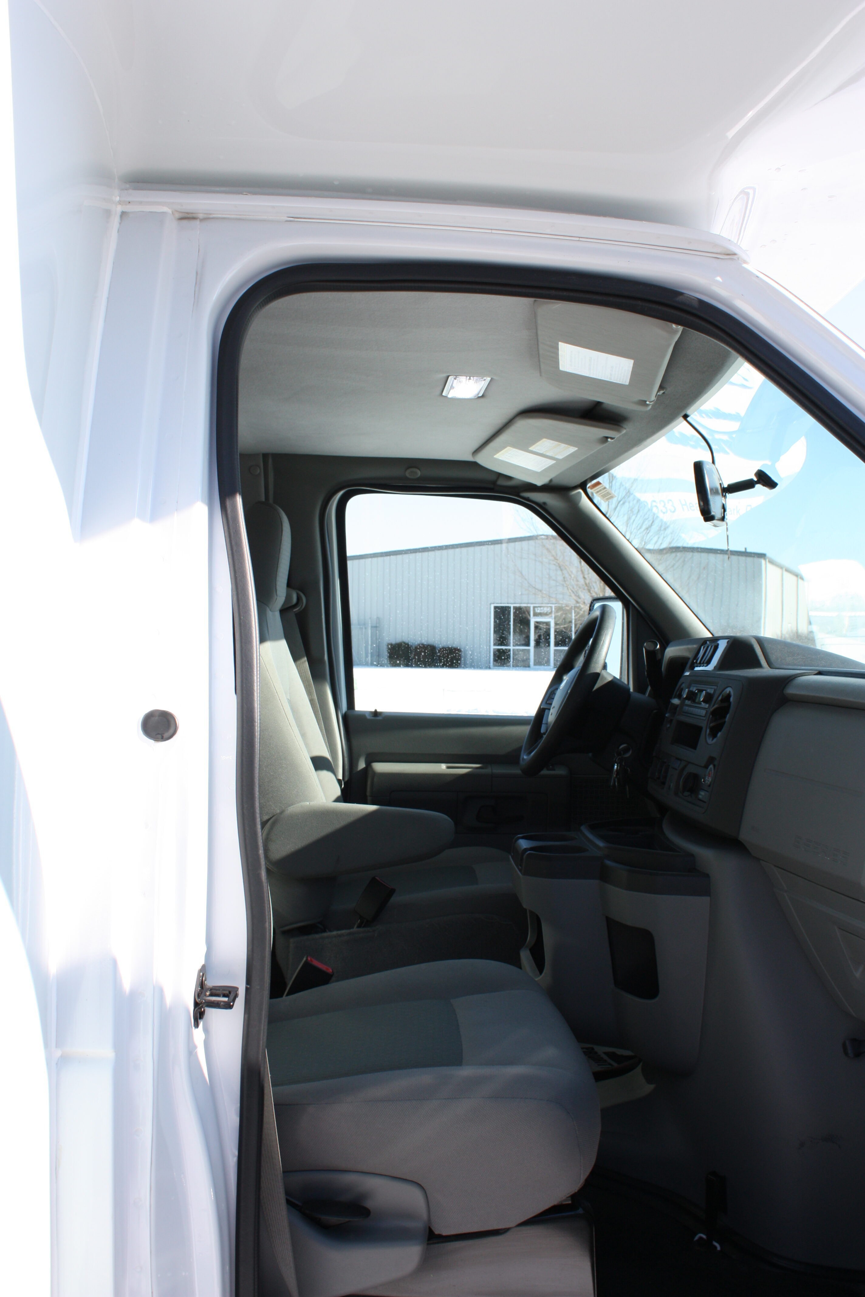 Open doorway into a white cargo van showing the driver’s seat, dashboard, and sun visors behind the door.