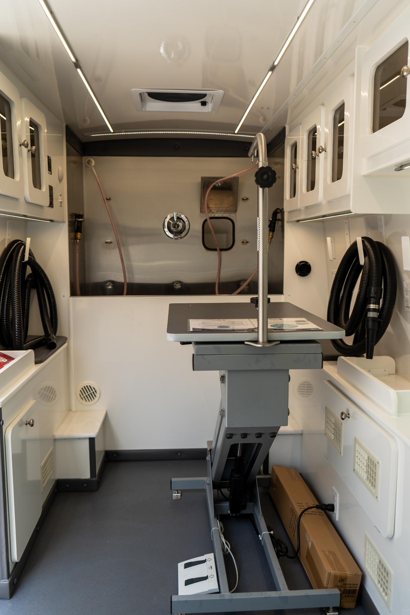 Interior of a white mobile clinic/ambulance with an adjustable treatment table and overhead cabinets, hoses coiled along the walls.
