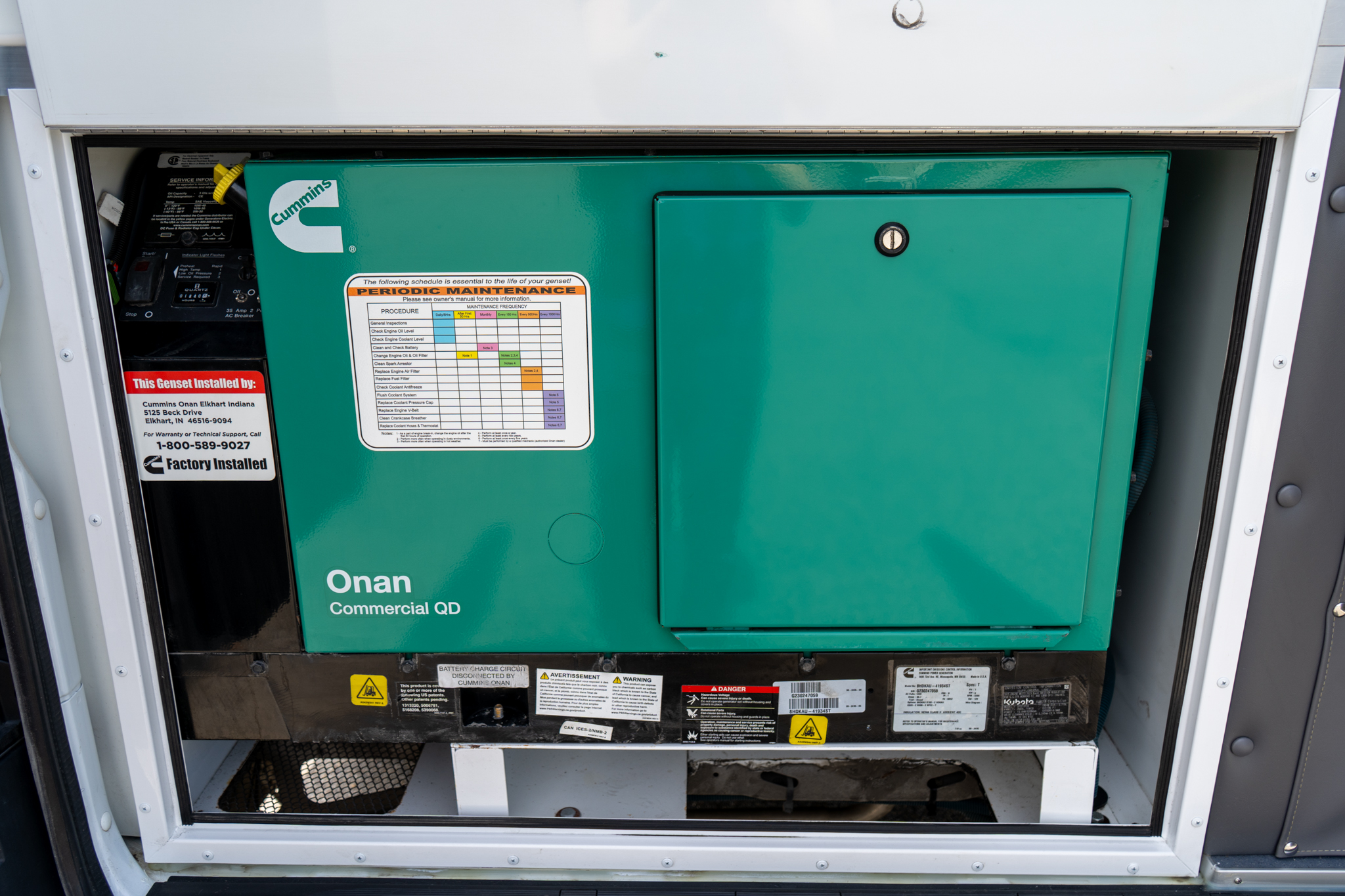 Green Cummins Onan commercial generator inside an open equipment compartment with maintenance label and warning stickers visible.
