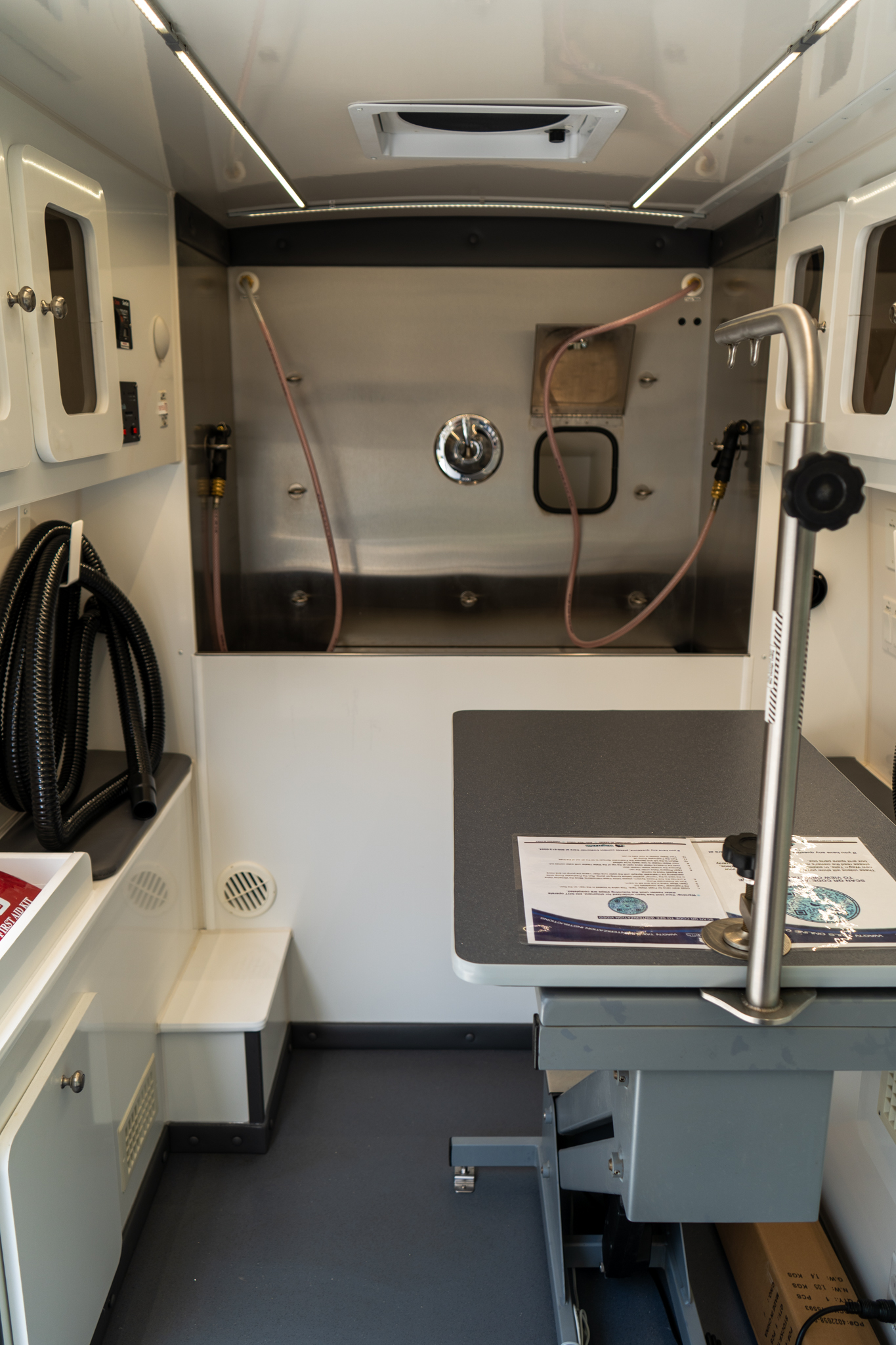 Interior of a compact stainless-steel cabinet with pink hoses attached to wall ports and a round gauge on the back panel.