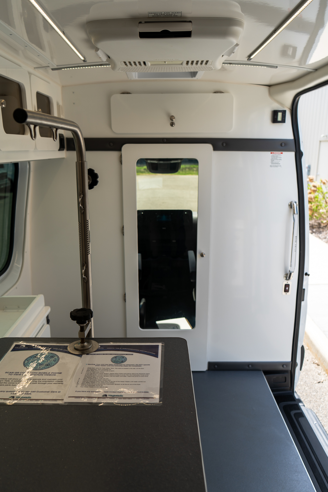 Interior of an ambulance showing a black countertop with a laminated instruction sheet and medical equipment mounted along the wall, door to the cabin visible in the background.