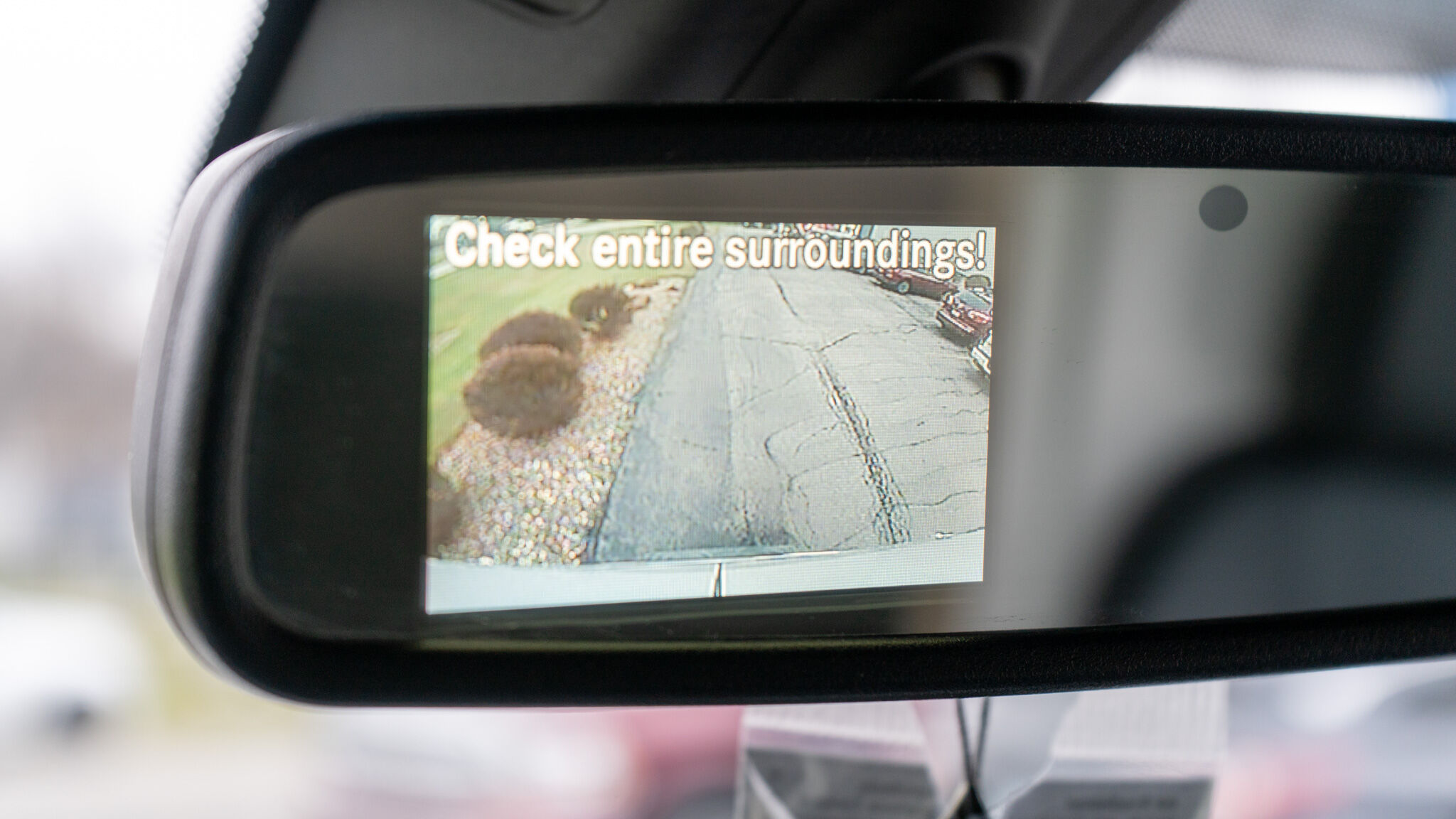 In-dash rearview mirror display showing a parking camera view with the warning 'Check entire surroundings!'