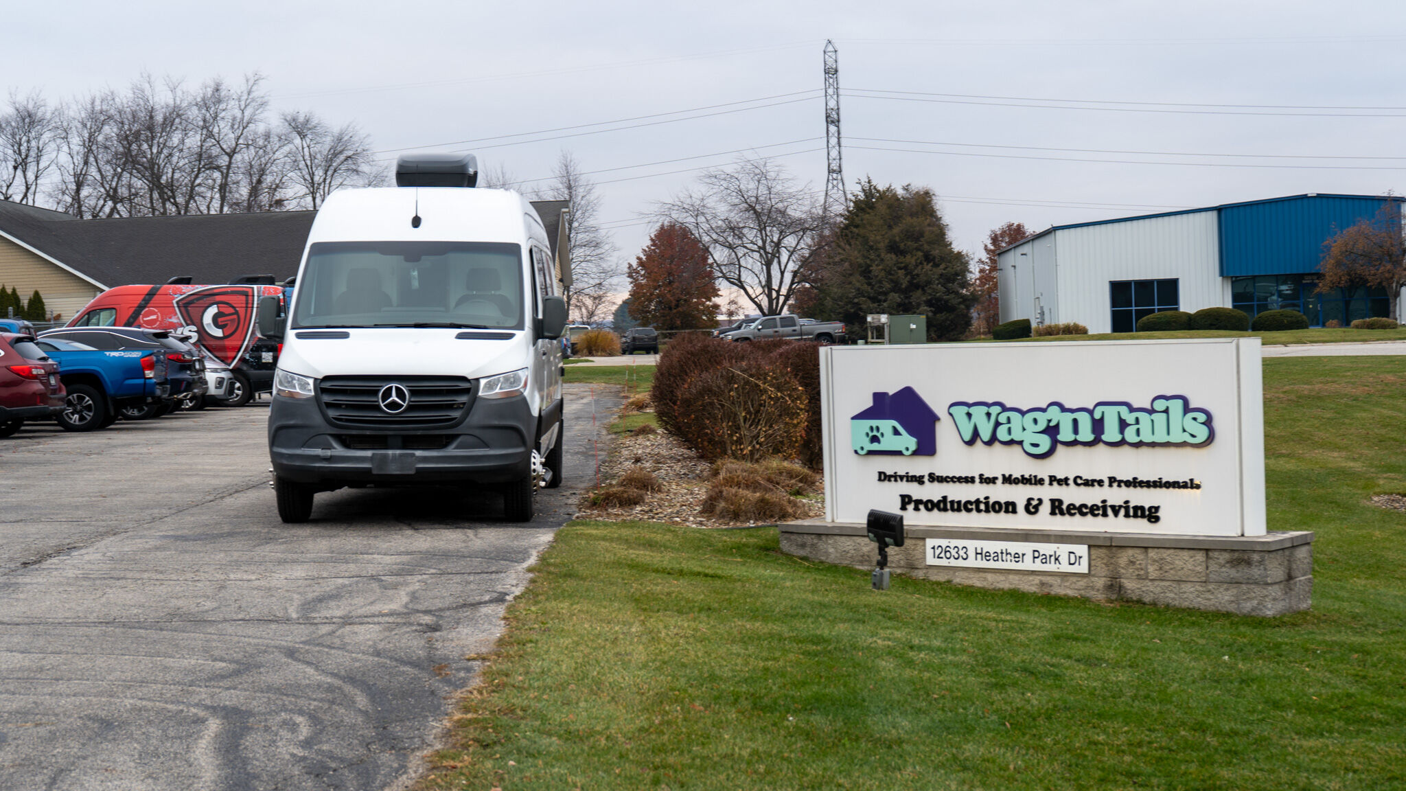 White Mercedes delivery van in a parking lot next to a Wag'n Tails sign advertising mobile pet care, Production & Receiving, with other vehicles nearby.