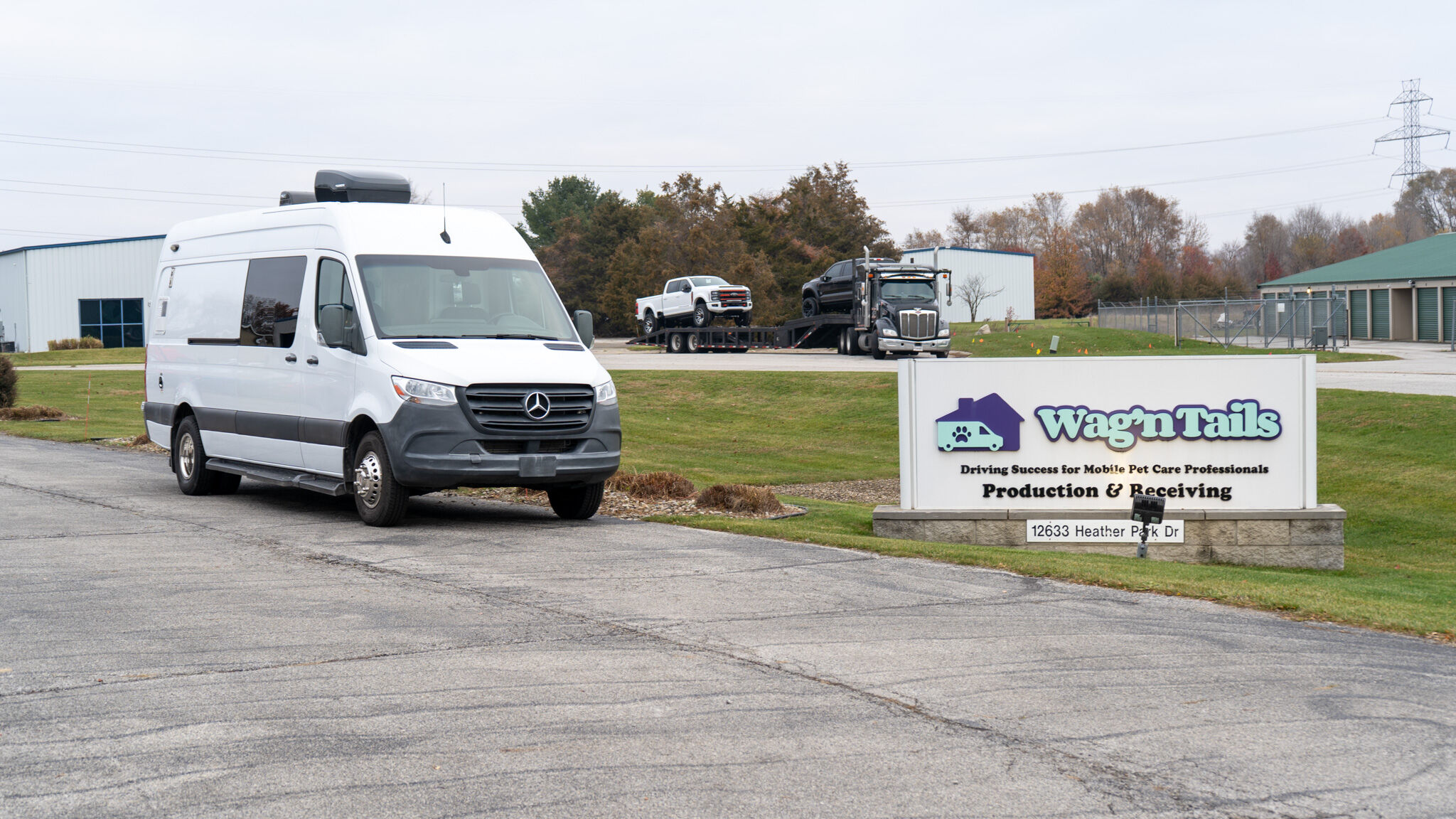 White Mercedes Sprinter van in the foreground at a business park, with a Wag'n Tails sign and service vehicles visible in the background.