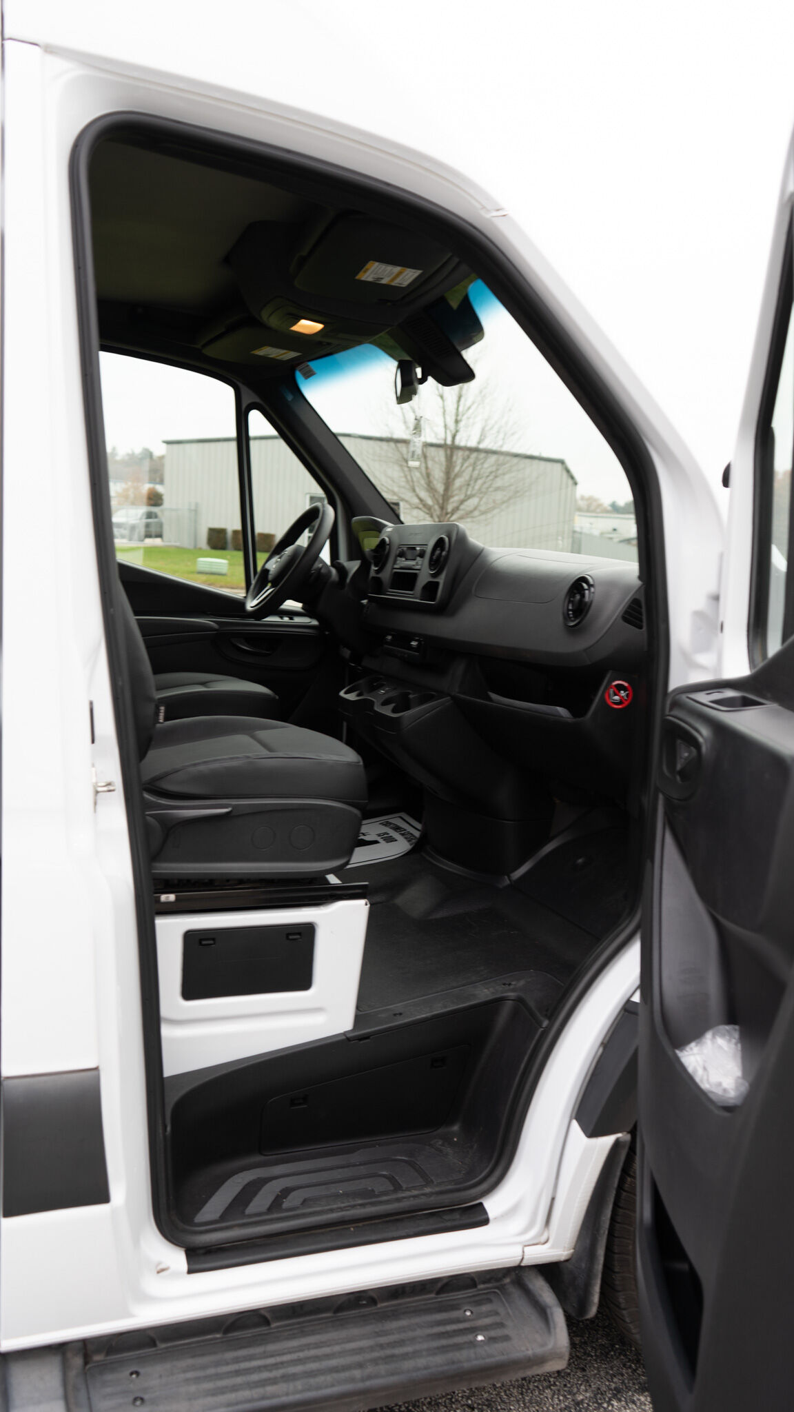 Interior of a white cargo van with driver and passenger seats, dashboard, and center console visible through open driver door