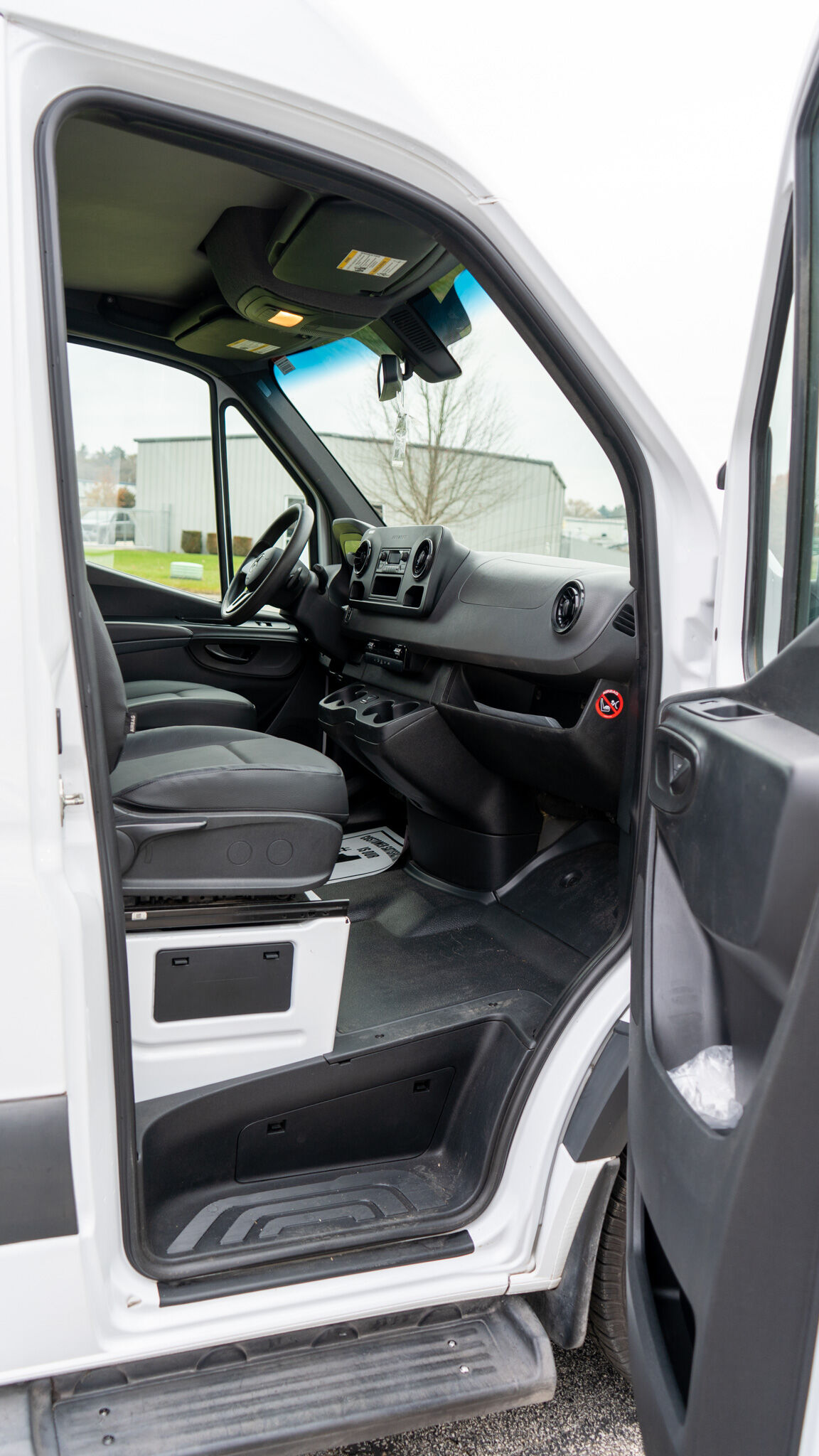 Open driver's door of a white van showing the dashboard, steering wheel, and front seats as seen from outside the cab.