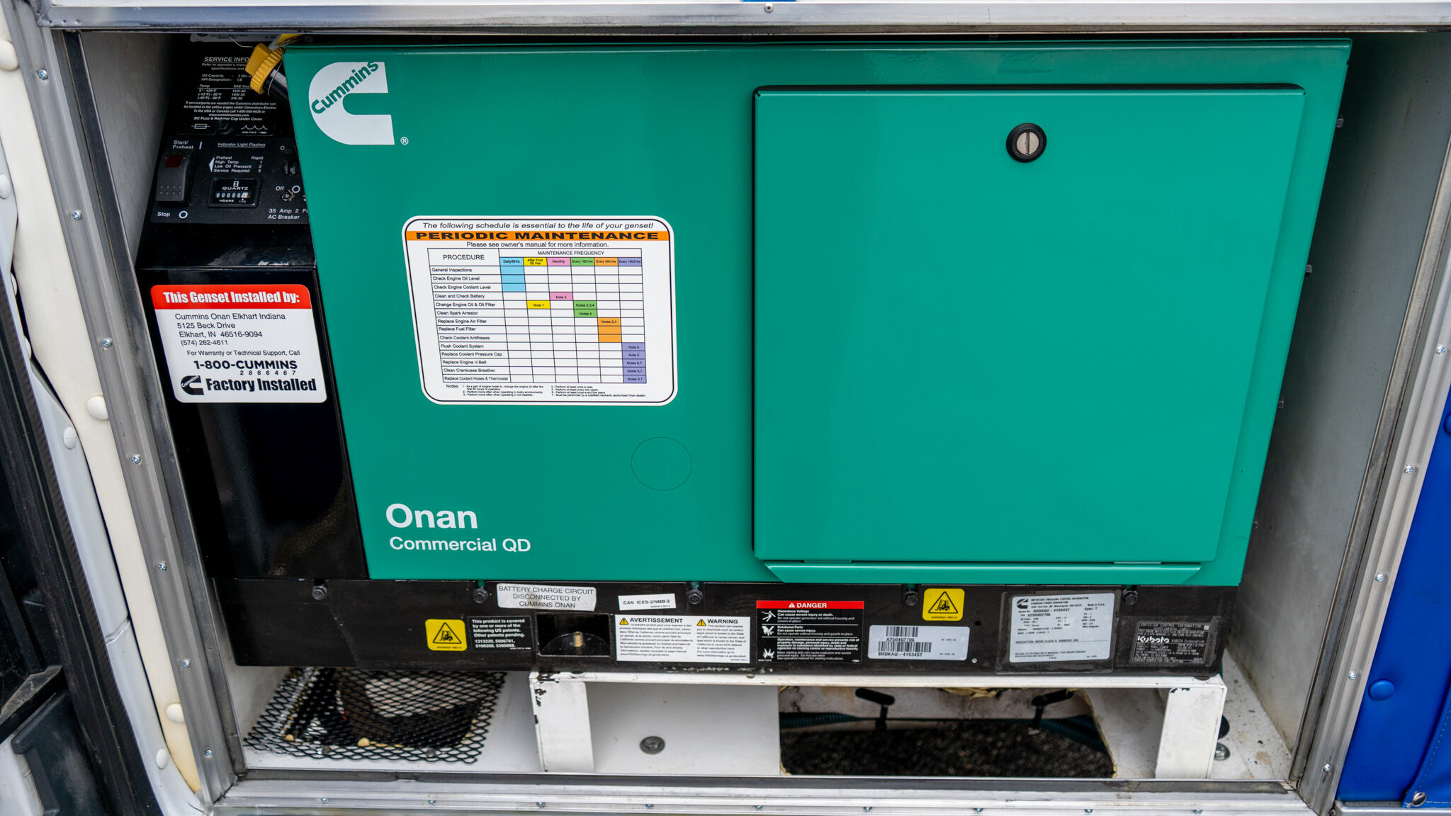 Green Cummins generator inside an access hatch with maintenance sticker and Onan Commercial QD label visible