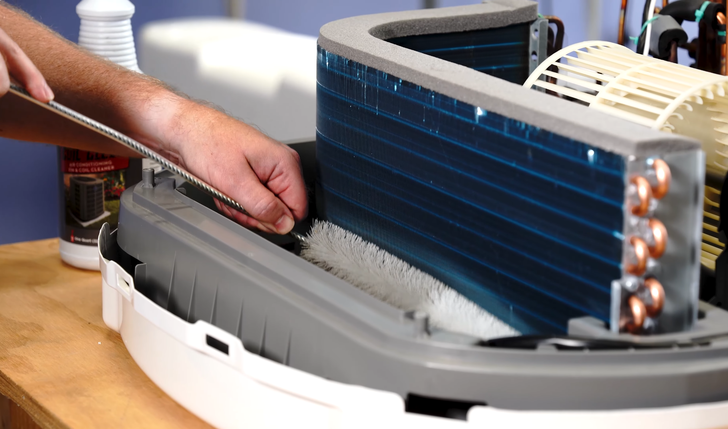 Hands of a technician servicing a split-system air conditioner, inserting a tool near the evaporator coil inside the indoor unit.