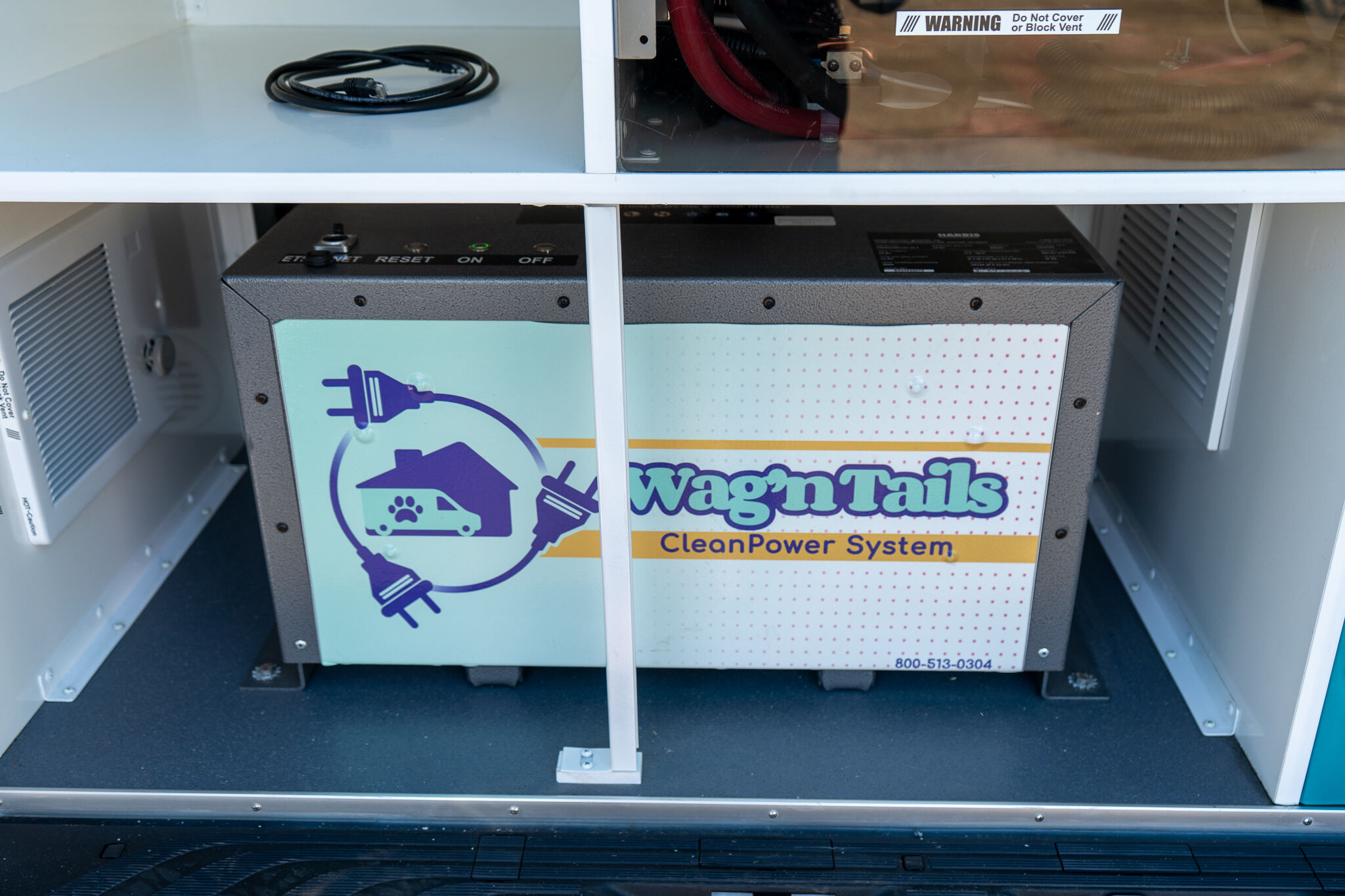 Power system cabinet labeled Wag'n Trails with a blue plug illustration on the front panel inside an open metal cabinet