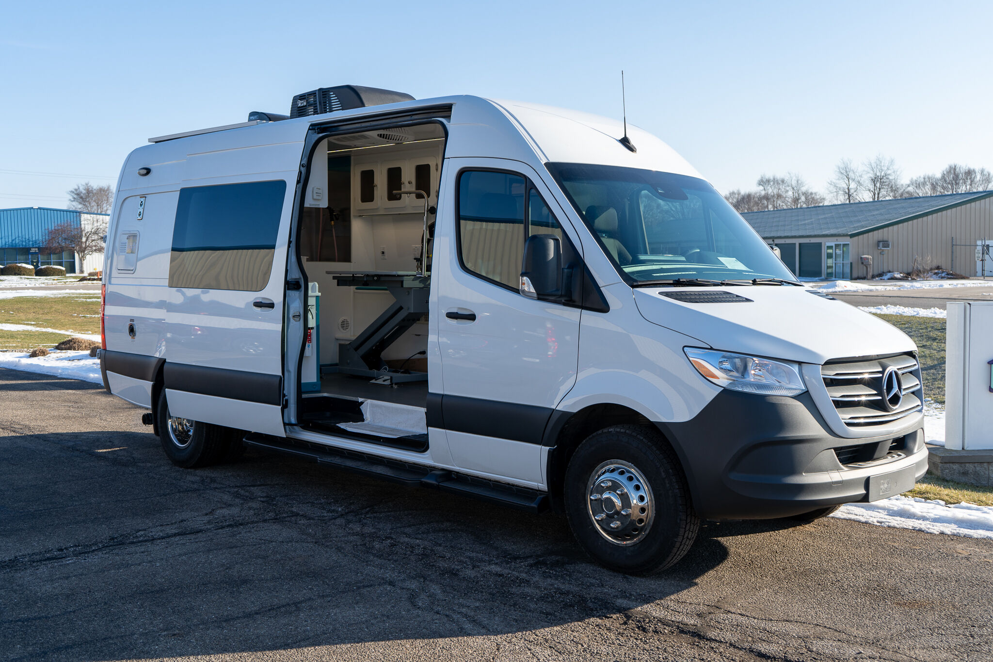 White commercial van with its side door open, revealing a workshop interior and equipment inside, outdoors on a sunny day