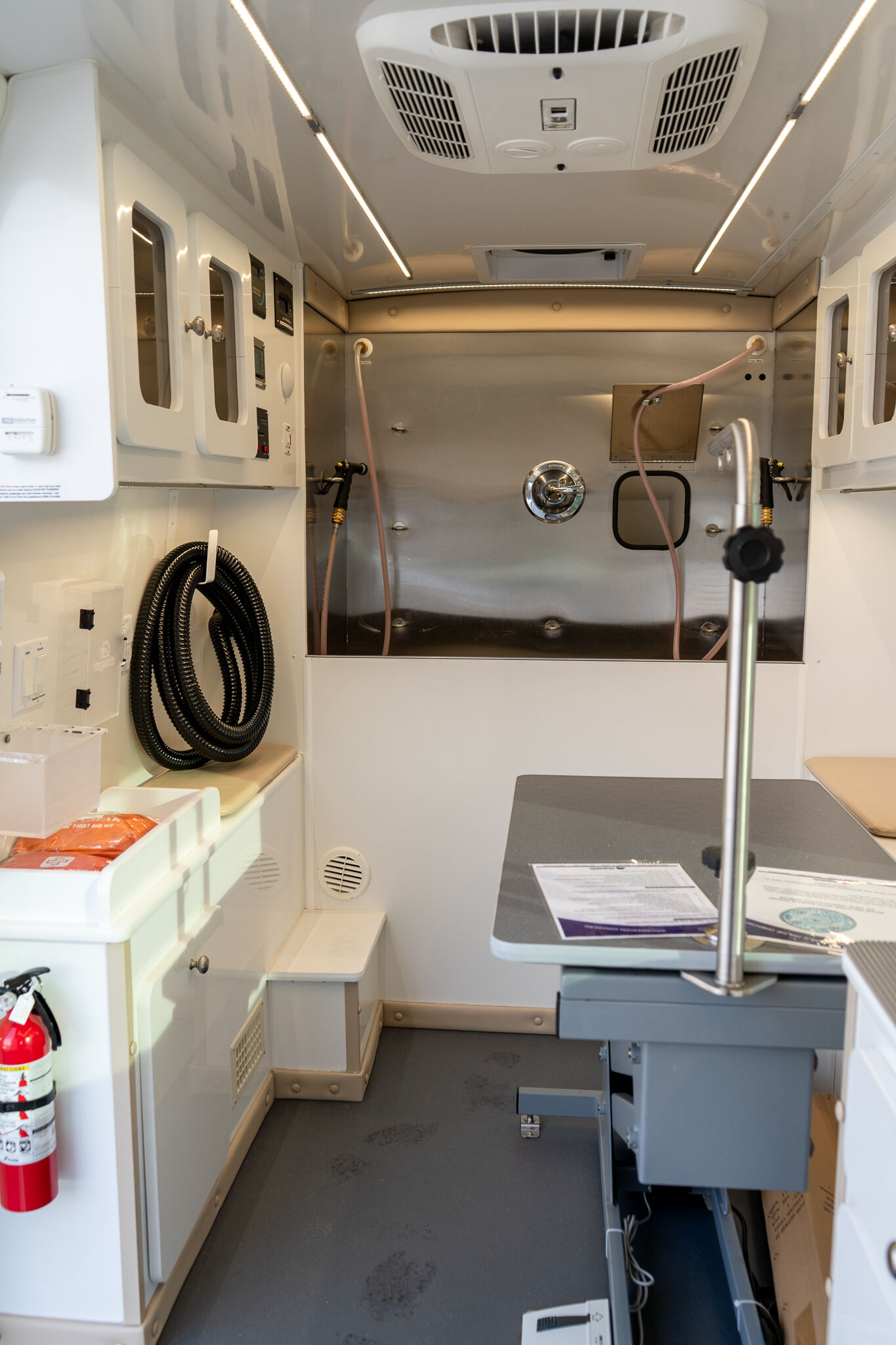 Interior of an ambulance showing wall-mounted medical cabinets, coiled hoses, and a stainless steel back wall with a mounted station for equipment.