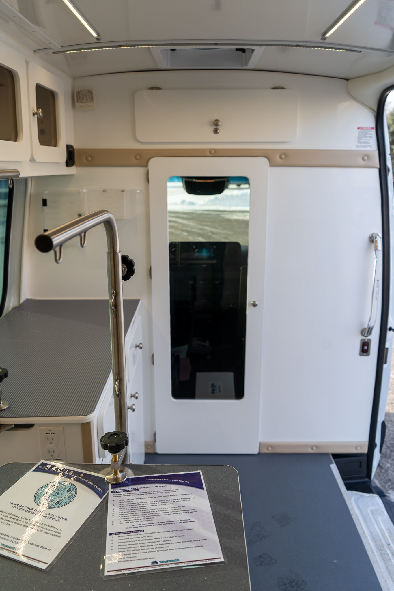 Interior of a white service van with a small kitchen area, cabinets, and a doorway to the outside viewed from the counter edge