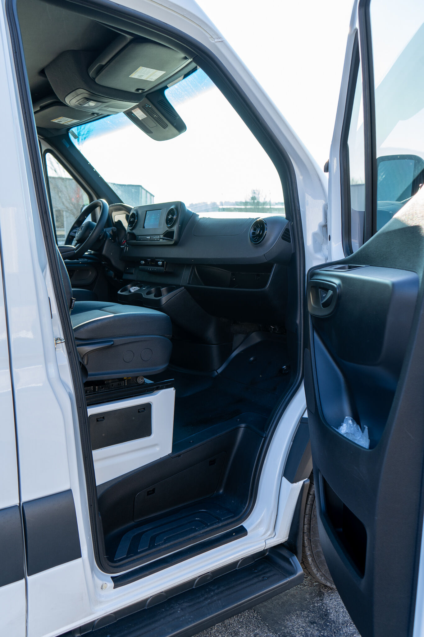 Open front cab of a white cargo van, showing the steering wheel, dashboard with touchscreen, and overhead console.