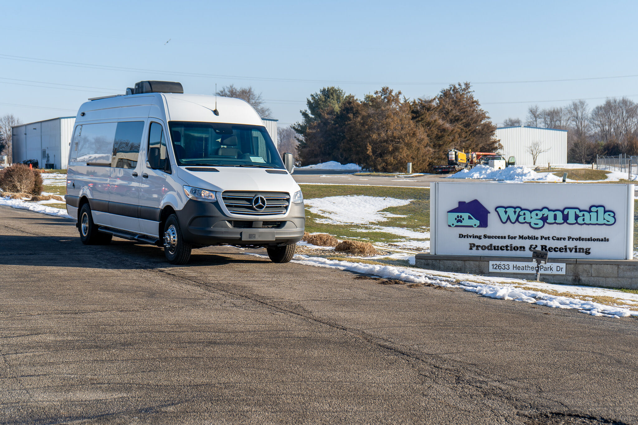 White Mercedes-Benz van parked in a lot beside a Wag'n Tails sign in a snowy, industrial area.