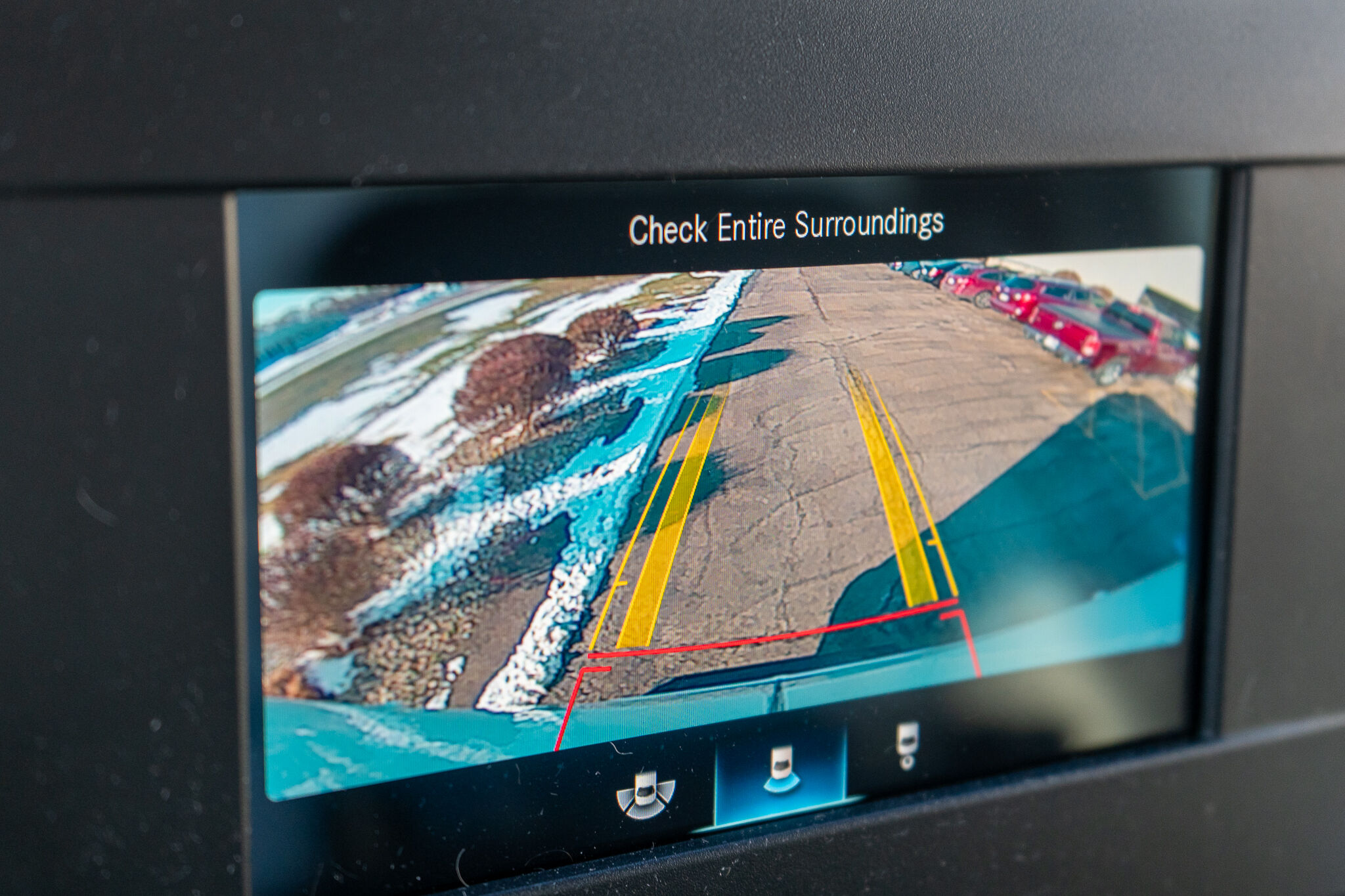 Car rearview camera screen showing view behind the vehicle with yellow guide lines and a