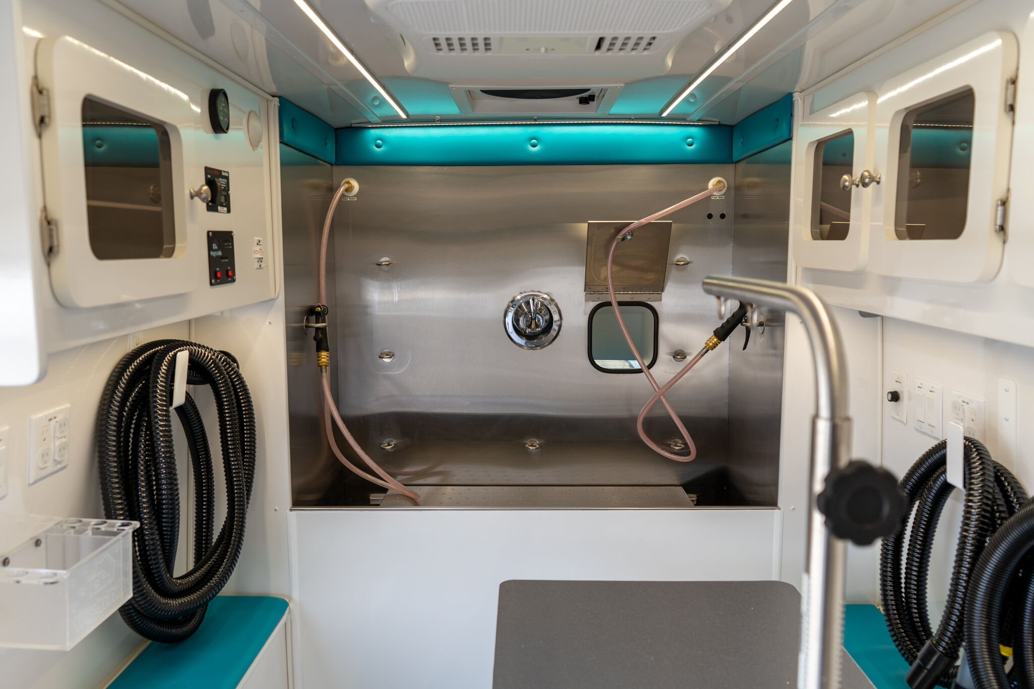 Interior of a small industrial or medical cabinet with stainless steel walls, teal padding, and coiled hoses; control panels on the left.