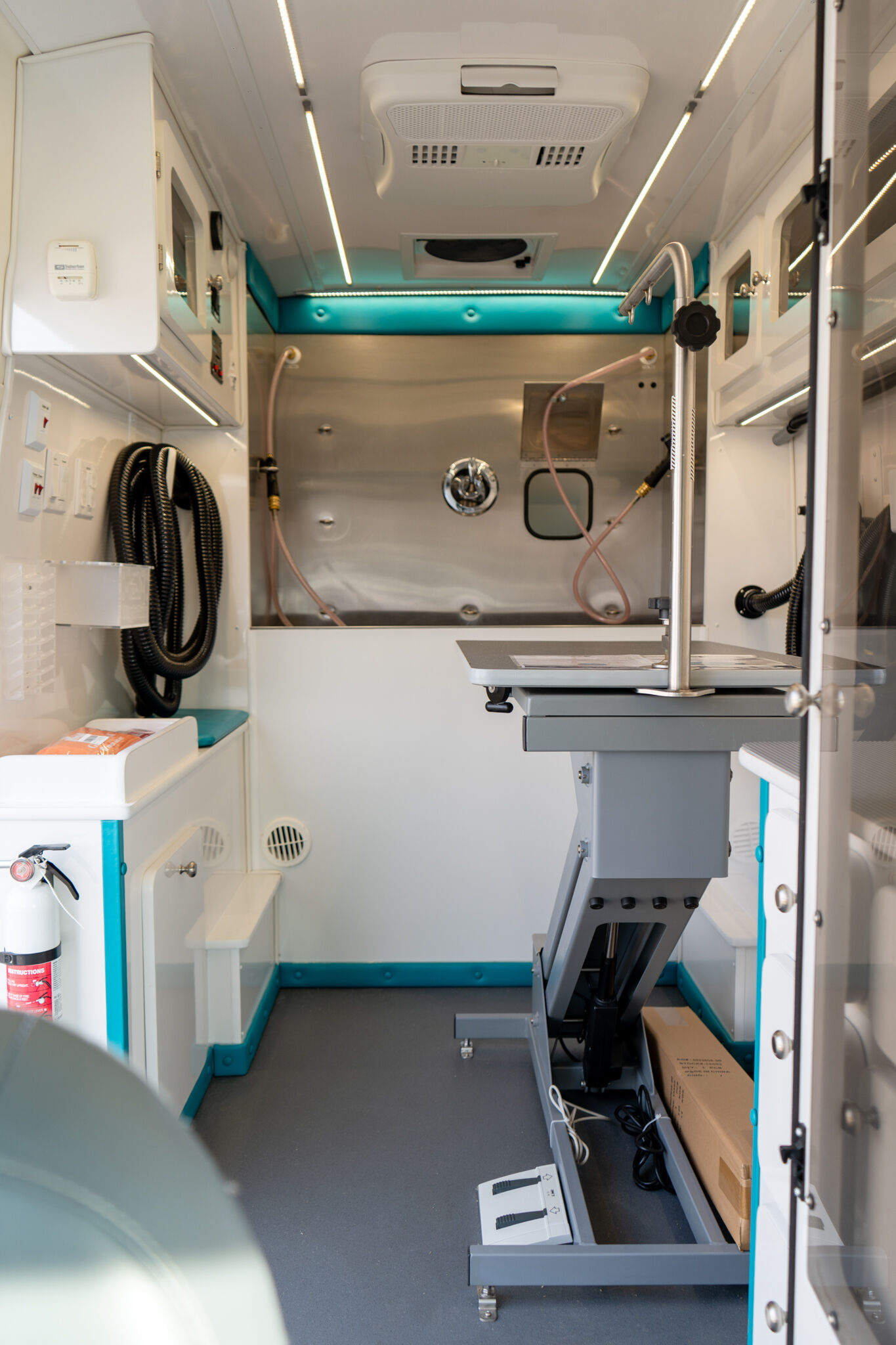 Interior of a medical ambulance workstation with shelves, cords, and a raised exam table in a clinical setting