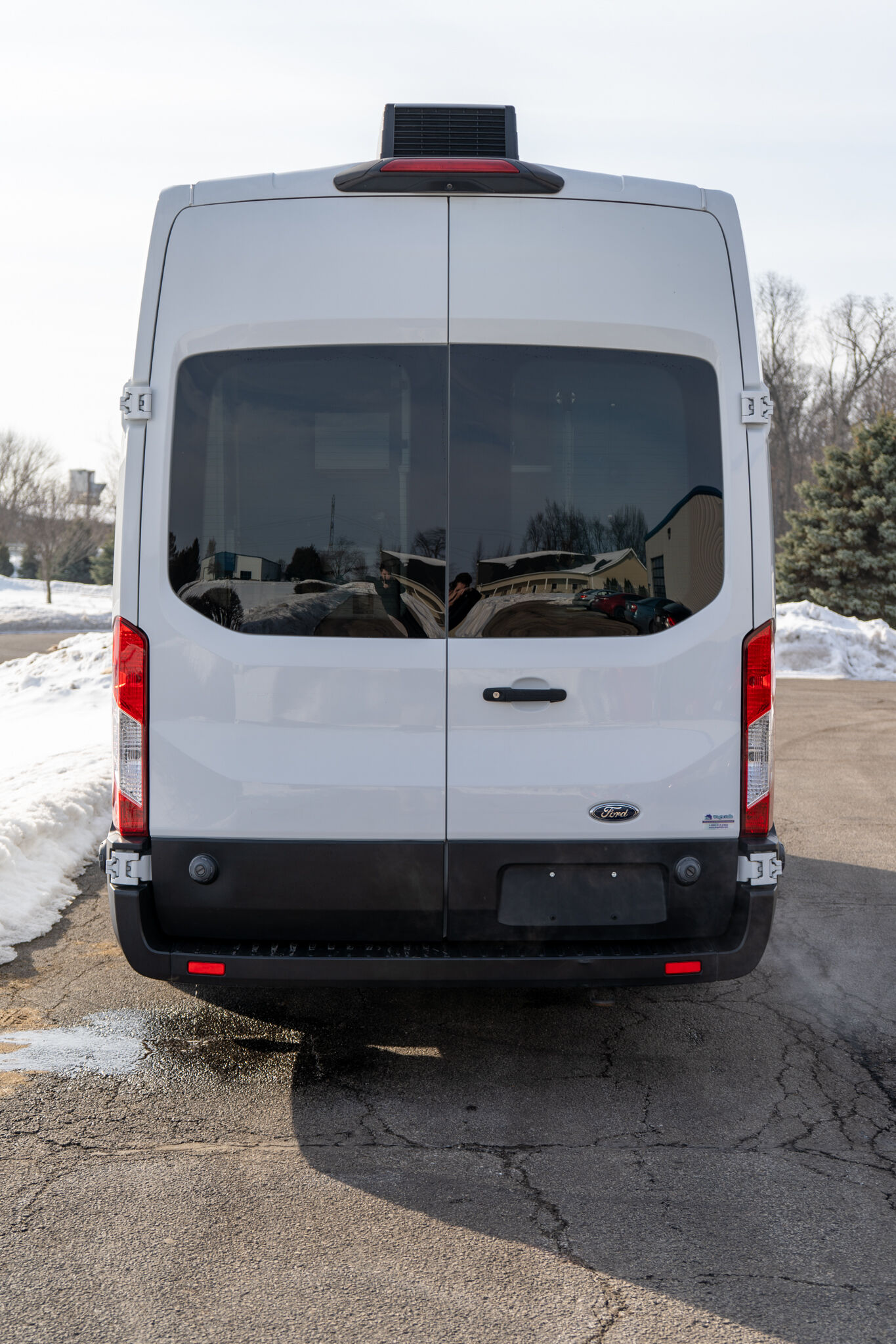 Rear view of a white Ford cargo van with double doors and dark rear windows, parked outdoors with snow nearby.