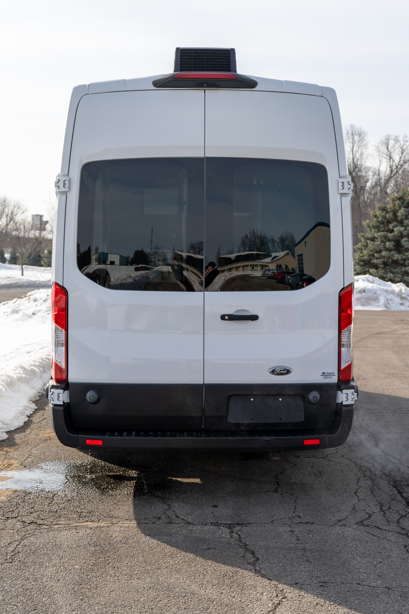 Rear view of a white Ford cargo van with double back doors and tinted windows in a snowy parking lot, daytime light.