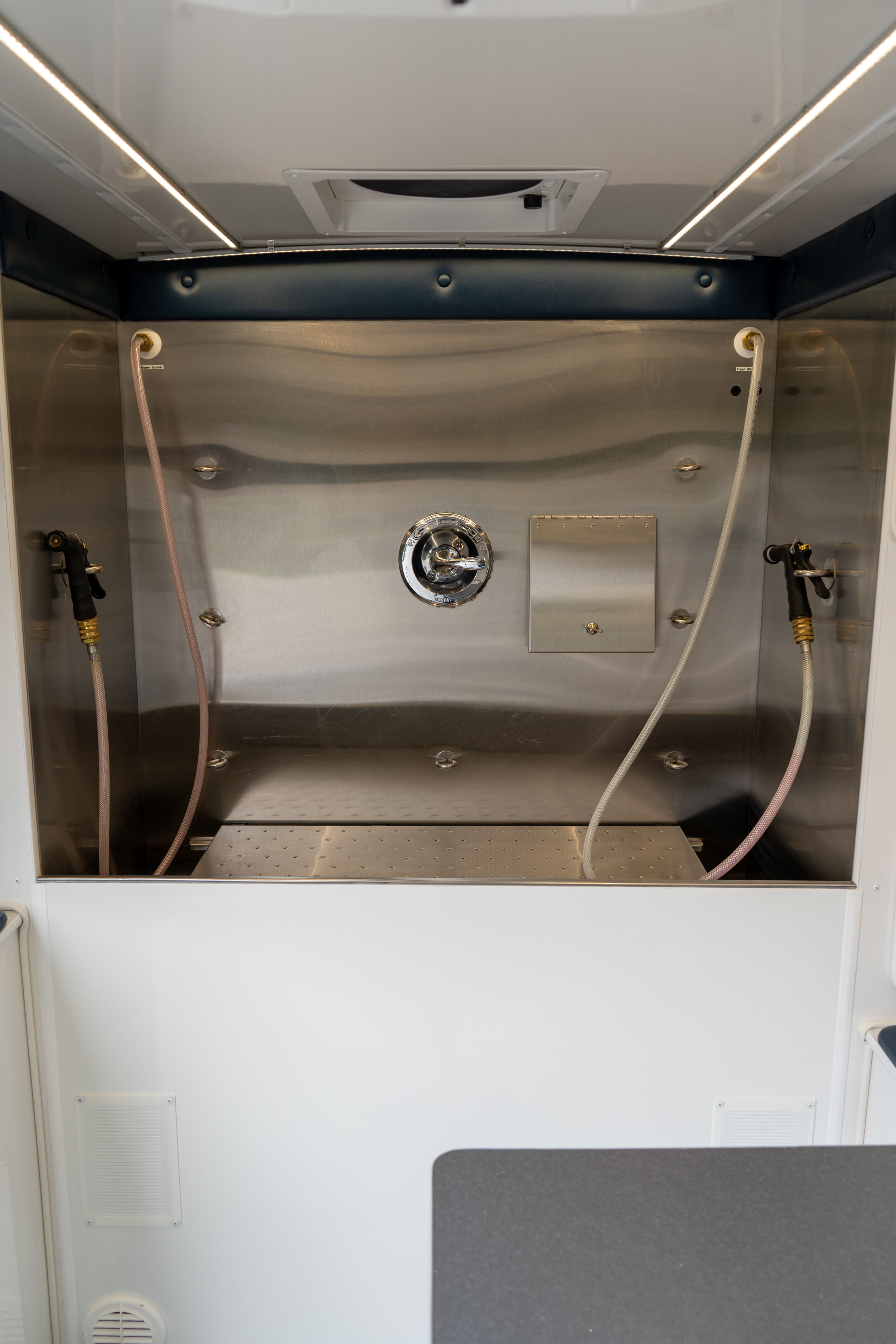Empty stainless steel wash booth with hoses on both sides and a round chrome control valve in the center.